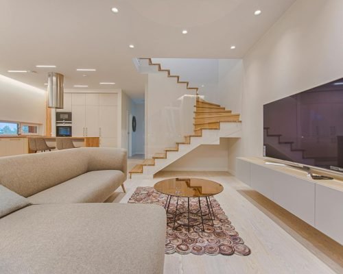Spacious modern living room featuring stairs, a TV, and sleek furniture design.